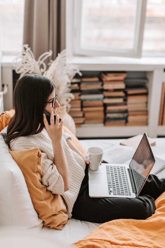 Young woman enjoying a cozy morning at home, using a laptop and sipping coffee.